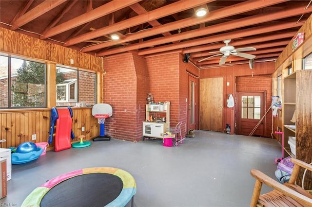 interior space featuring lofted ceiling with beams, a ceiling fan, wood walls, brick wall, and concrete flooring