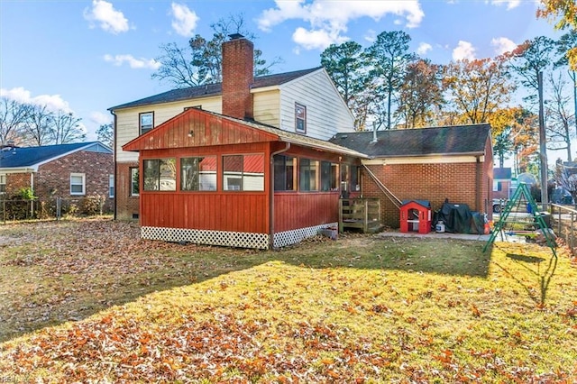 back of house featuring a sunroom, a yard, a chimney, and brick siding