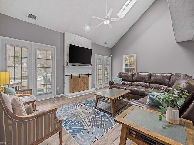 living area featuring a skylight, visible vents, a ceiling fan, wood finished floors, and high vaulted ceiling