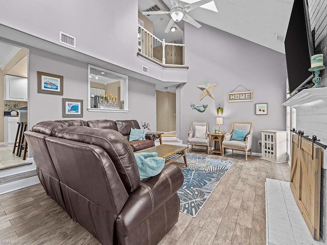 living room with a towering ceiling, a ceiling fan, visible vents, and wood finished floors