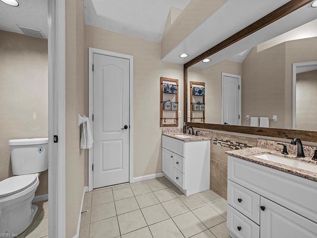 bathroom featuring two vanities, toilet, a sink, a textured ceiling, and tile patterned flooring