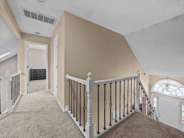 hallway featuring carpet floors, visible vents, and an upstairs landing