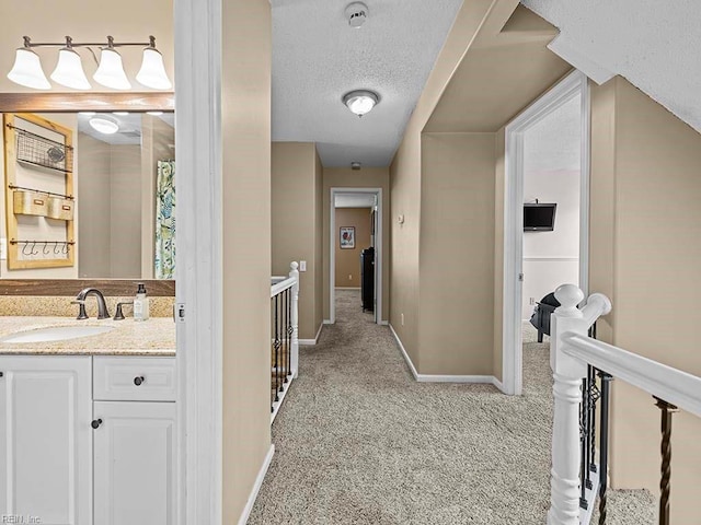 hall with a textured ceiling, a sink, an upstairs landing, and light colored carpet