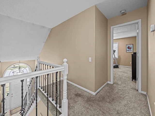 hall featuring a textured ceiling, carpet flooring, an upstairs landing, baseboards, and vaulted ceiling