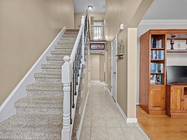 staircase featuring tile patterned flooring, crown molding, a textured ceiling, and baseboards