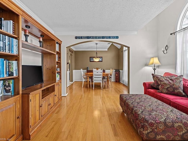 living room featuring light wood-type flooring, crown molding, arched walkways, and a textured ceiling