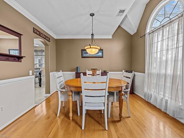 dining room featuring light wood-style floors, arched walkways, visible vents, and a textured ceiling