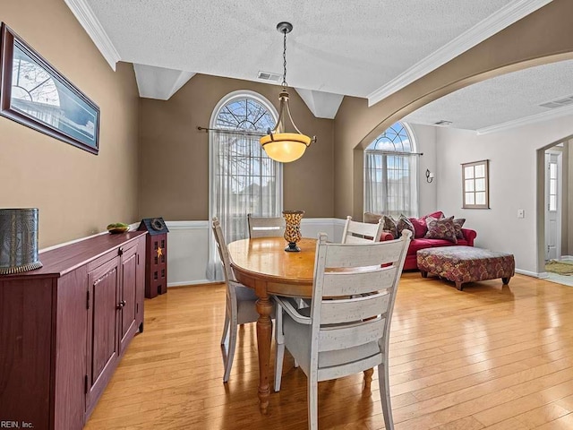 dining area featuring arched walkways, light wood-type flooring, visible vents, and crown molding