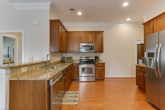 kitchen featuring visible vents, light wood-style flooring, appliances with stainless steel finishes, brown cabinetry, and a sink