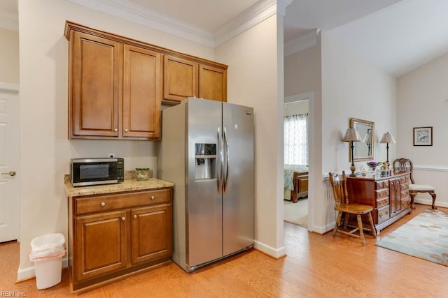 kitchen with light stone counters, stainless steel appliances, brown cabinetry, ornamental molding, and light wood-type flooring