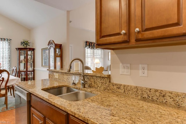 kitchen featuring light stone counters, brown cabinets, vaulted ceiling, stainless steel dishwasher, and a sink