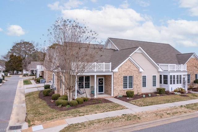 view of front of house featuring brick siding, roof with shingles, a porch, and a balcony