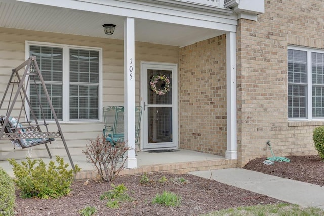 entrance to property featuring a porch and brick siding