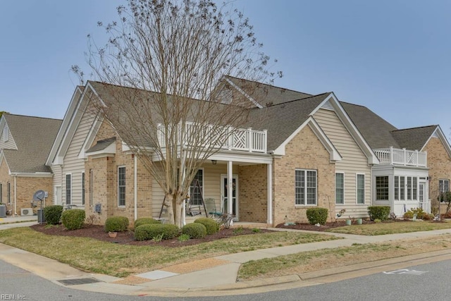 view of front of house with brick siding, a porch, a balcony, and a shingled roof