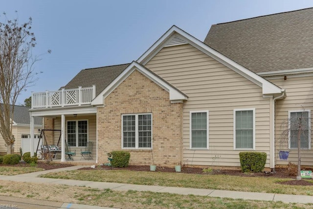 view of front of property with a porch, brick siding, a shingled roof, and a balcony