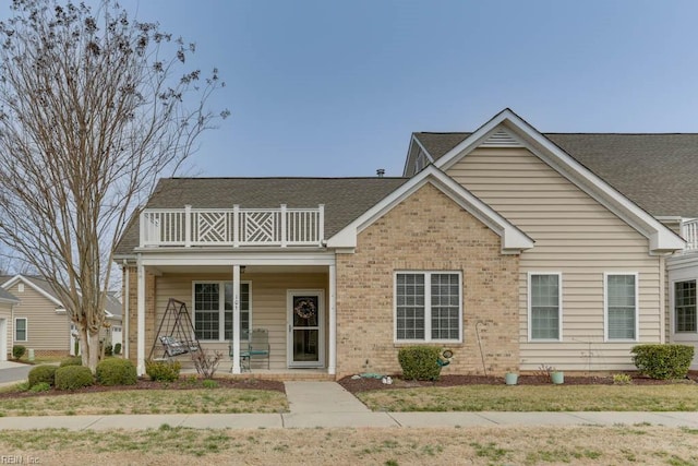 view of front of house featuring a balcony, roof with shingles, a porch, and brick siding