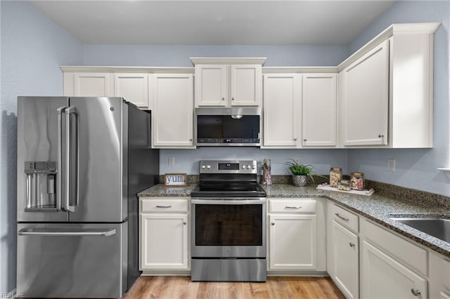 kitchen with stainless steel appliances, light wood-style flooring, stone countertops, and white cabinetry