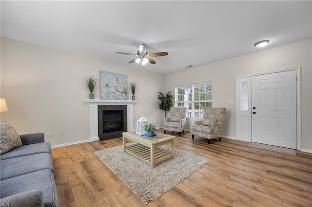 living room with a ceiling fan, a glass covered fireplace, baseboards, and wood finished floors