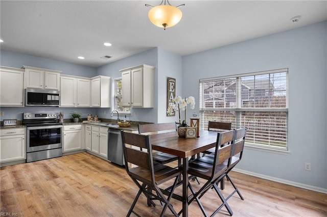 kitchen with a sink, white cabinets, baseboards, appliances with stainless steel finishes, and light wood finished floors