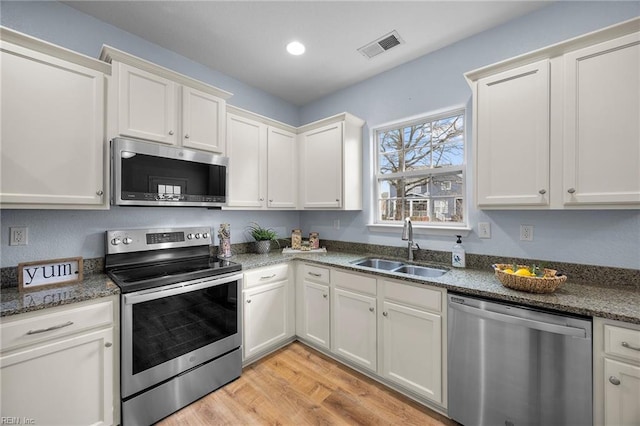 kitchen featuring stainless steel appliances, a sink, visible vents, white cabinets, and light wood-style floors