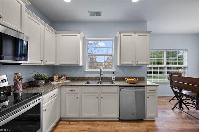 kitchen with stainless steel appliances, visible vents, white cabinets, a sink, and dark stone countertops