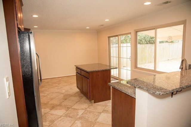 kitchen with ornamental molding, visible vents, brown cabinetry, and freestanding refrigerator