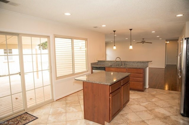 kitchen featuring a center island, brown cabinets, freestanding refrigerator, a sink, and dark stone countertops