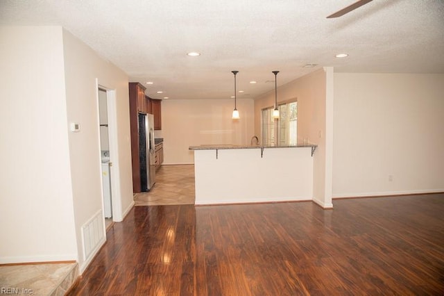 kitchen featuring a peninsula, a breakfast bar, dark wood-type flooring, and freestanding refrigerator