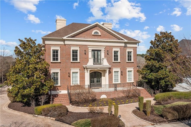 georgian-style home featuring covered porch, brick siding, and a chimney