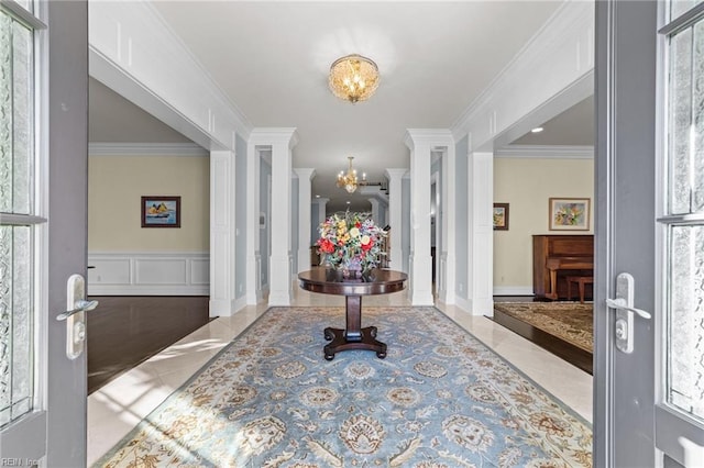 entrance foyer with a chandelier, crown molding, a decorative wall, and ornate columns