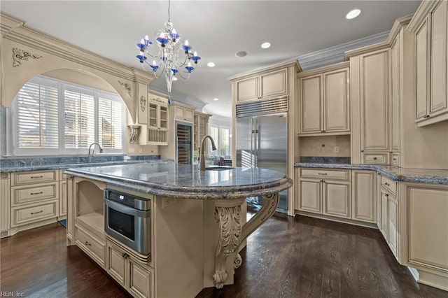 kitchen with stainless steel appliances, a sink, cream cabinetry, dark stone counters, and dark wood finished floors