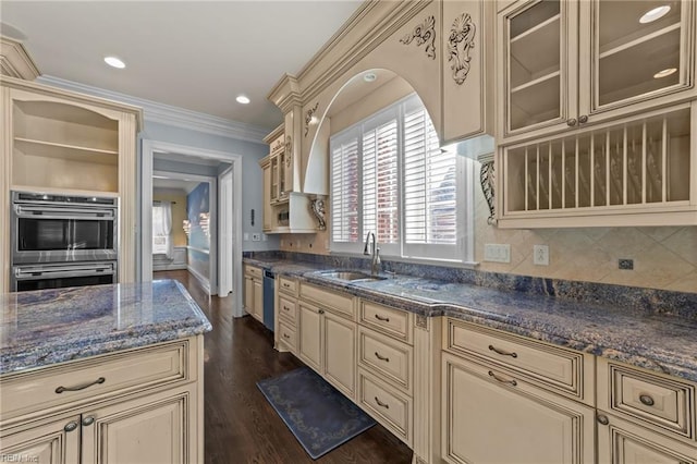 kitchen with cream cabinetry, crown molding, stainless steel appliances, glass insert cabinets, and a sink