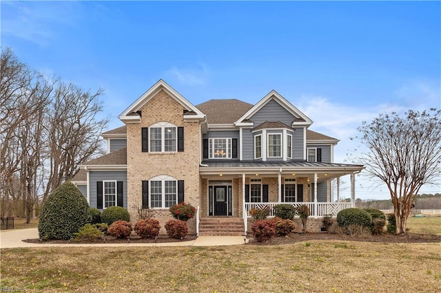 view of front of home with a shingled roof, a front yard, covered porch, and brick siding