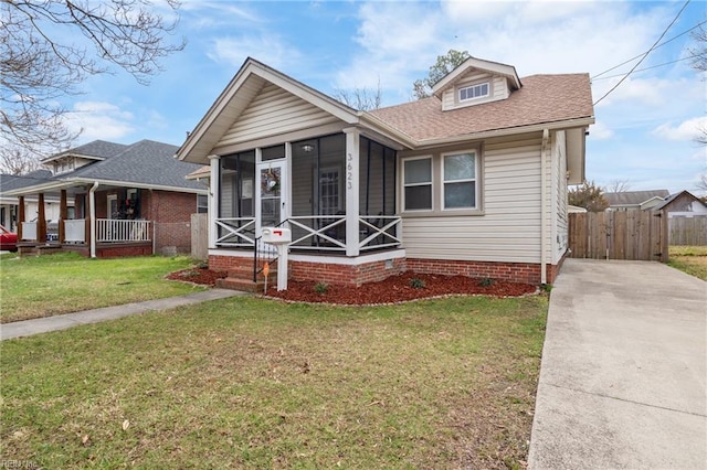 bungalow with a shingled roof, a front yard, a sunroom, and fence