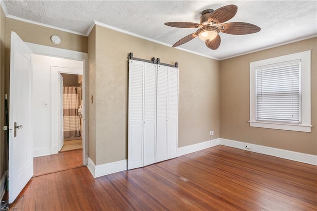 unfurnished bedroom with a barn door, ornamental molding, a textured ceiling, wood finished floors, and baseboards