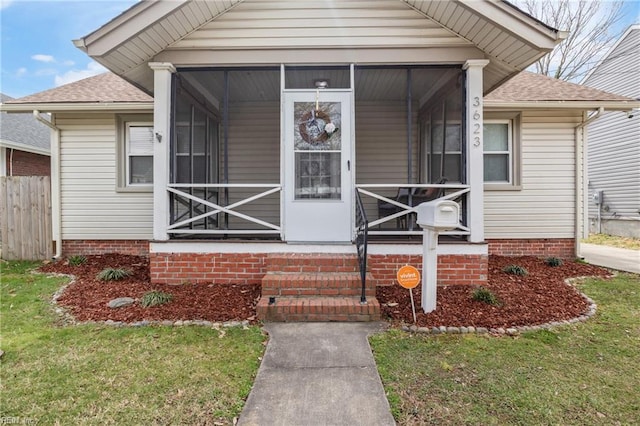 entrance to property with a yard, fence, a porch, and roof with shingles