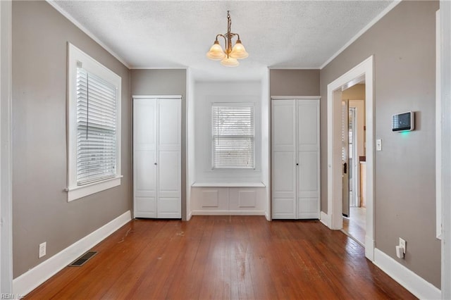 unfurnished bedroom featuring baseboards, wood-type flooring, visible vents, and two closets