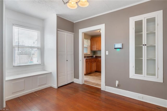 interior space with a textured ceiling, a notable chandelier, dark wood-style flooring, baseboards, and crown molding