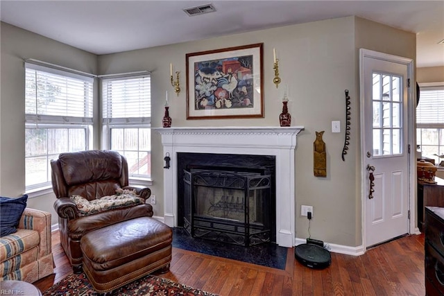 living area with a fireplace with flush hearth, baseboards, visible vents, and hardwood / wood-style floors