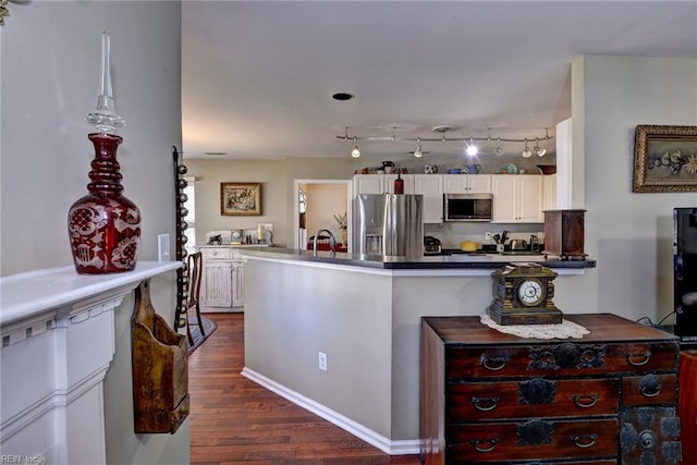 kitchen with stainless steel appliances, a peninsula, a sink, white cabinets, and dark wood-style floors