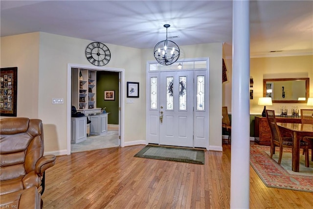 entrance foyer with decorative columns, light wood-style flooring, baseboards, and an inviting chandelier