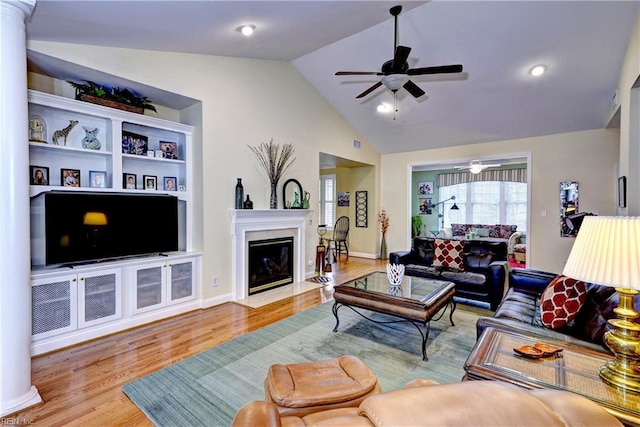 living room featuring lofted ceiling, a fireplace with flush hearth, ceiling fan, wood finished floors, and ornate columns