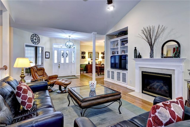 living room with built in features, a fireplace, decorative columns, vaulted ceiling, and wood finished floors