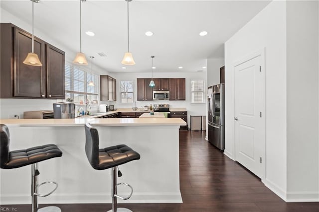 kitchen featuring stainless steel appliances, light countertops, dark wood-type flooring, dark brown cabinetry, and a peninsula