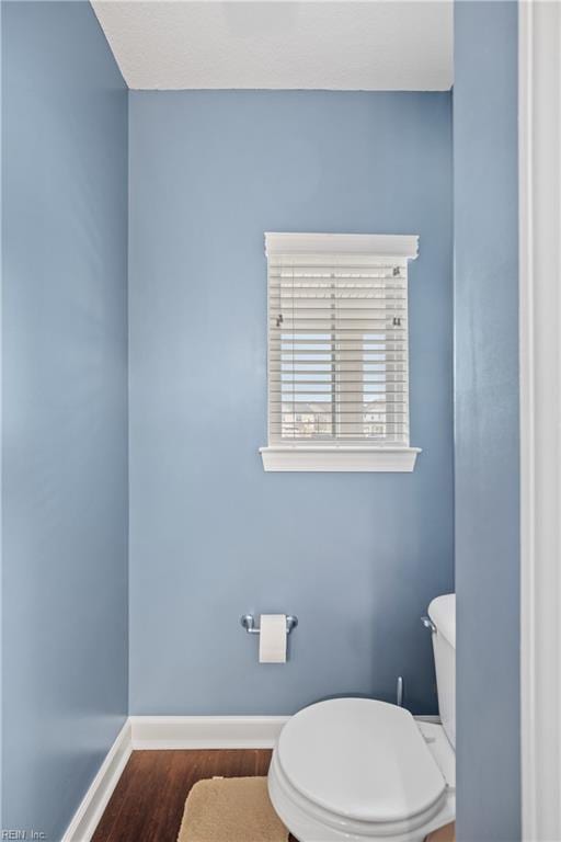 half bathroom featuring baseboards, toilet, and wood finished floors