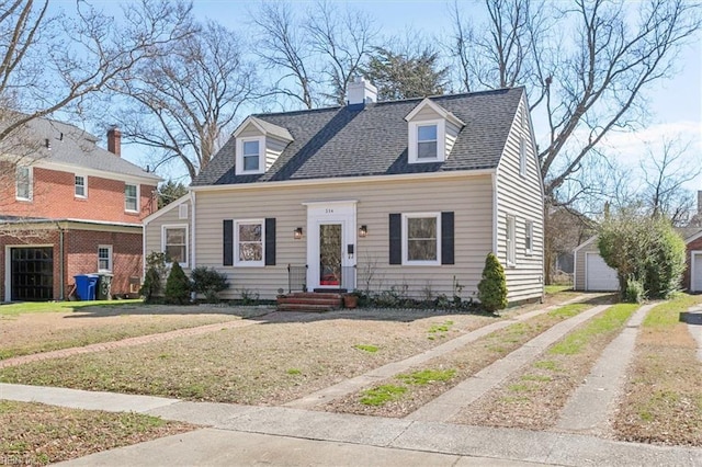 new england style home featuring driveway, a shingled roof, a chimney, an outdoor structure, and a front yard