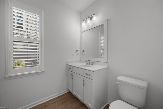 half bath featuring baseboards, vanity, toilet, and wood finished floors