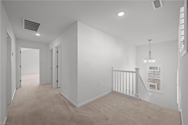 hallway with light carpet, an upstairs landing, visible vents, and an inviting chandelier