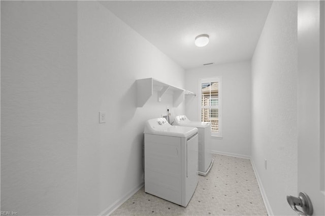 washroom featuring a textured wall, laundry area, baseboards, light floors, and washer and clothes dryer