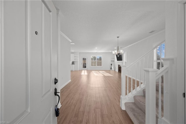 entryway featuring a textured ceiling, light wood-style floors, stairway, an inviting chandelier, and crown molding